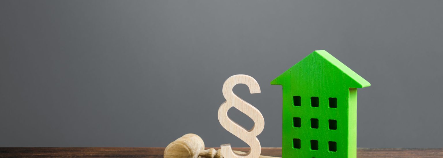 Green house and paragraph figurine with a judge hammer. Litigation in housing and real estate disputes. Norms and rules for construction, maintenance. Encouraging green and energy-saving technologies.
